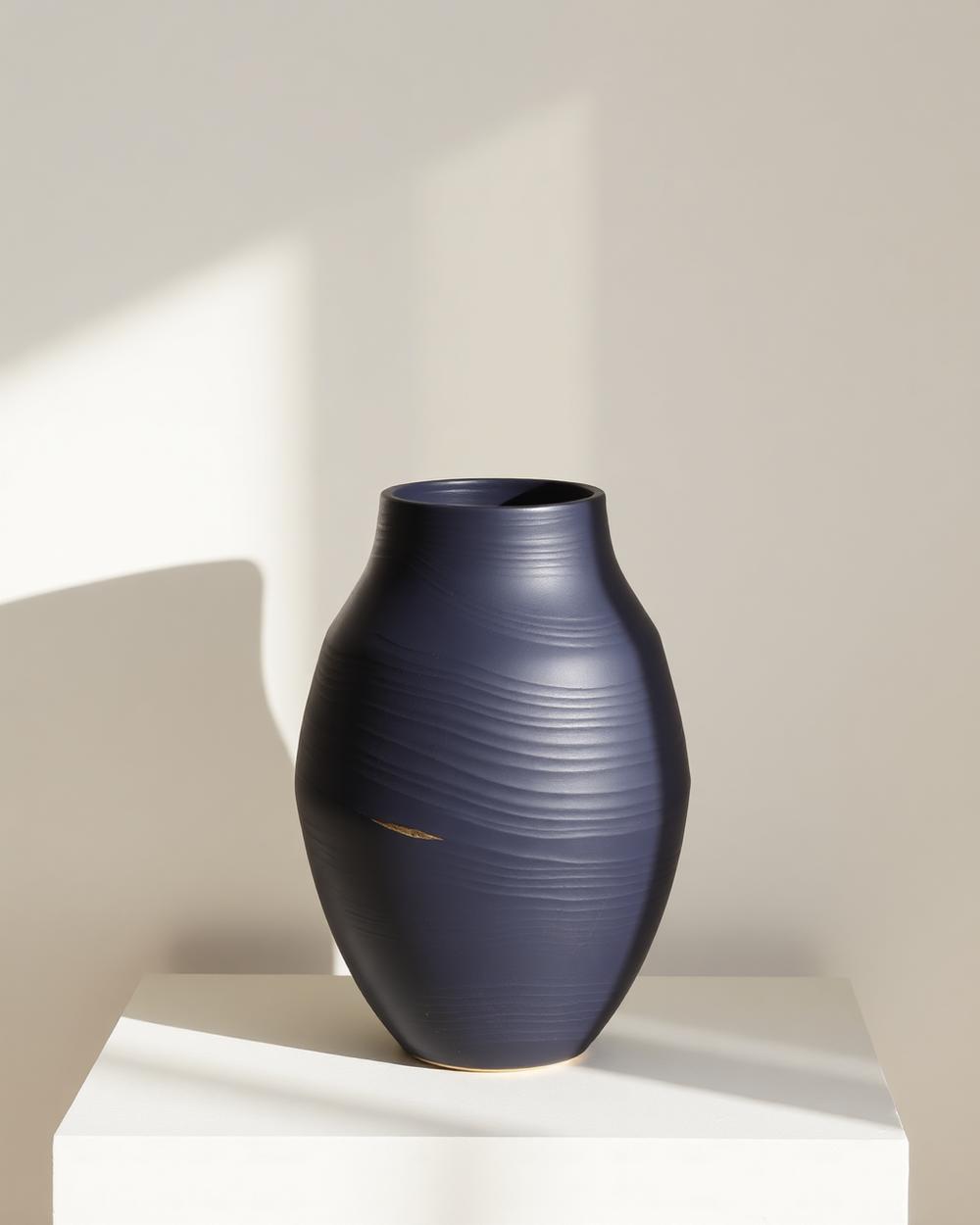 Matte navy ceramic vessel with a rippled surface and a single fine brass seam