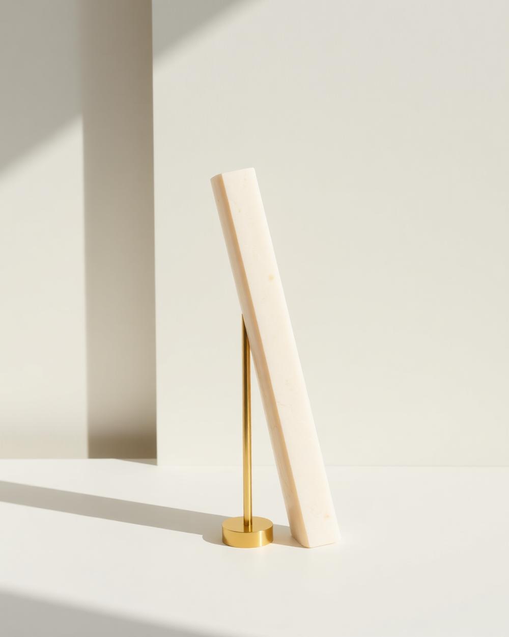 Tall pale stone column held in balance by a slender brass rod