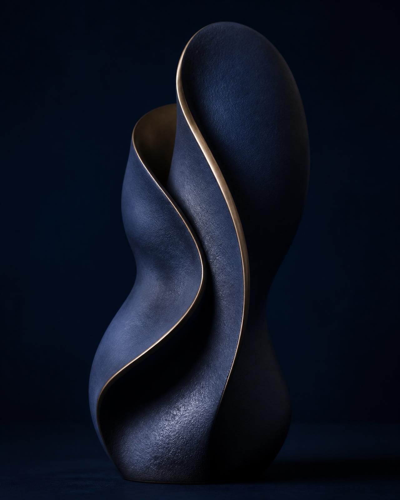 Sculptural navy ceramic form curving around itself, edged with a single fine brass line