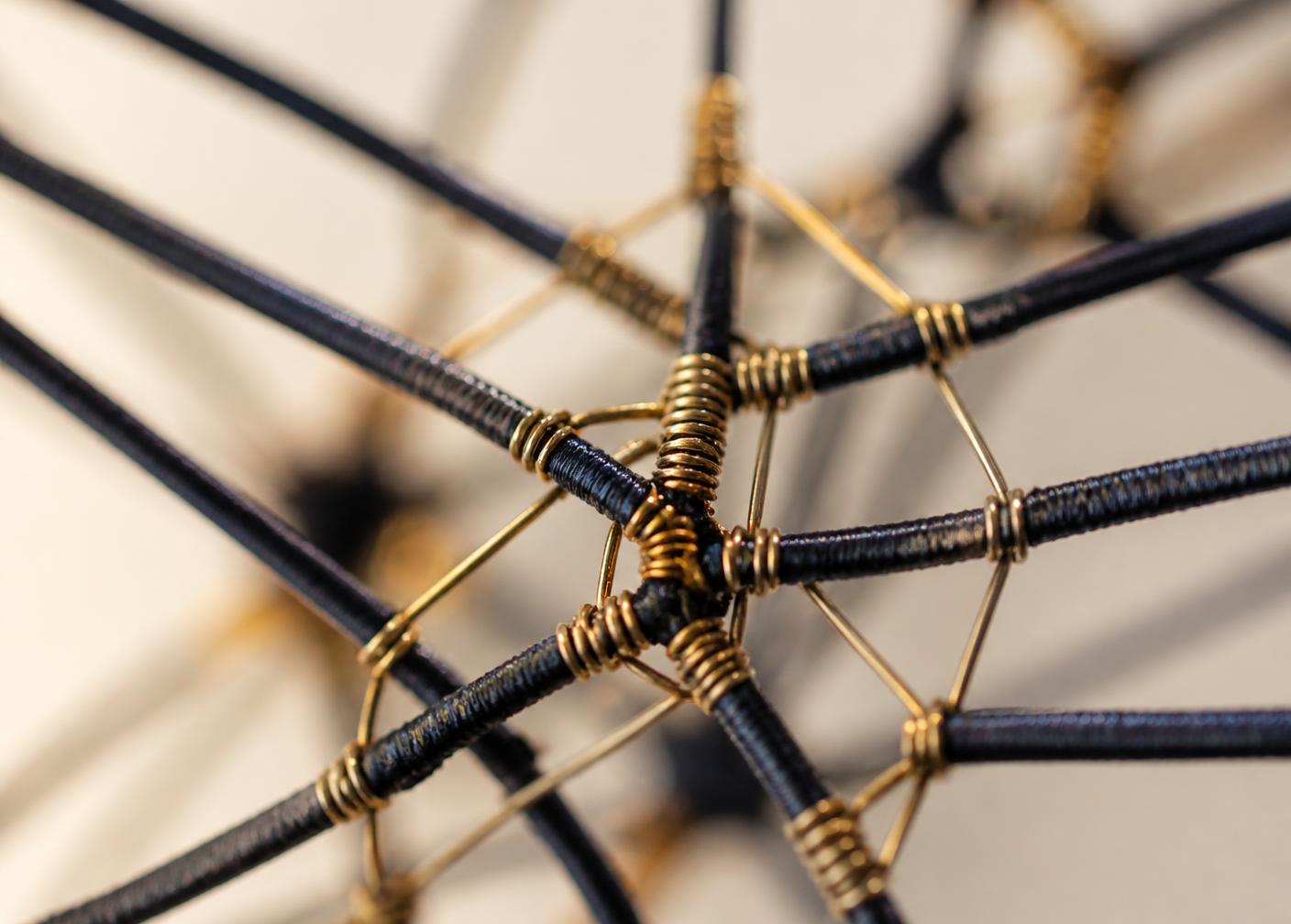 Macro view of navy cords bound with fine brass wire converging at a single connected node